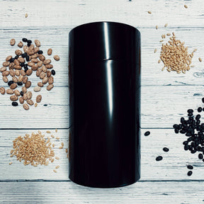 Black medium seed storage vault container surrounded by assorted seeds on wooden surface